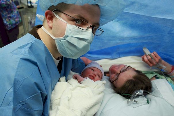 Stan Lemon in surgical gown holding newborn Lucy in the delivery room, November 2009
